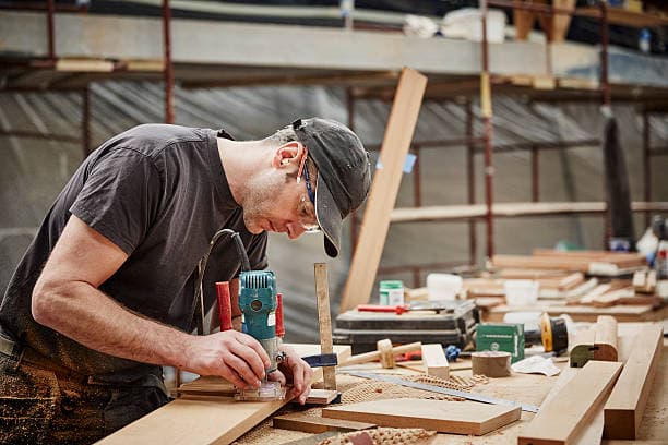 Carpenter hand-planing a deck board with sawdust catching the light
